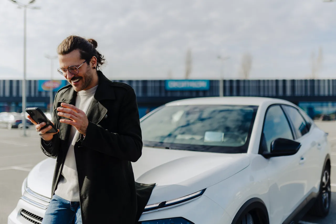 Junger Fahrer mit Smartphone an seinem Auto
