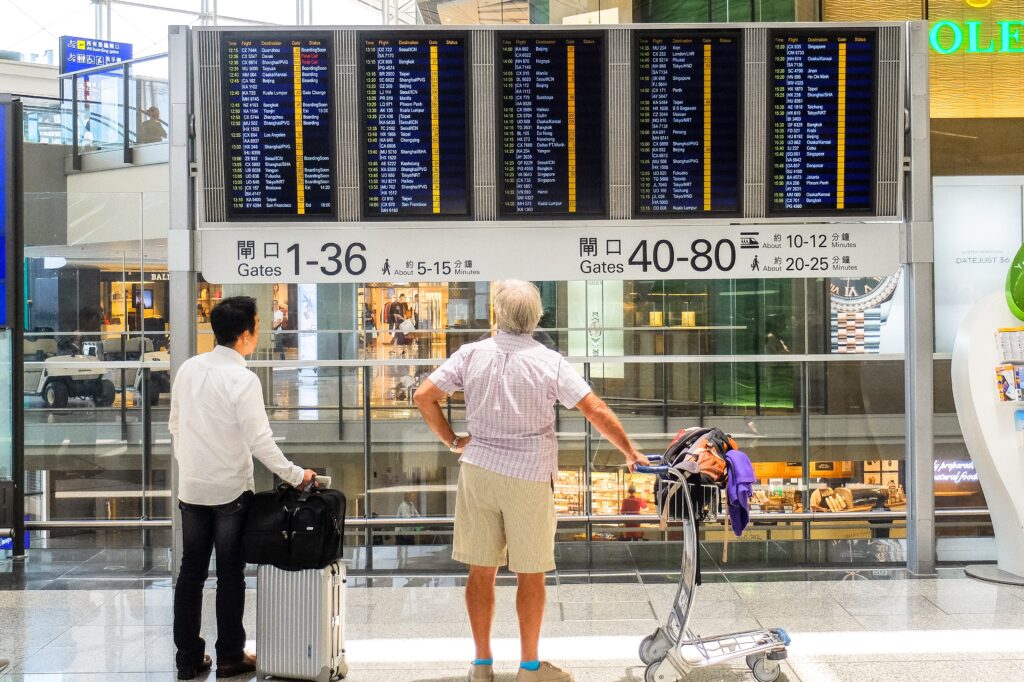 zwei männliche personen stehen am flughafen und schauen auf die flugtafel