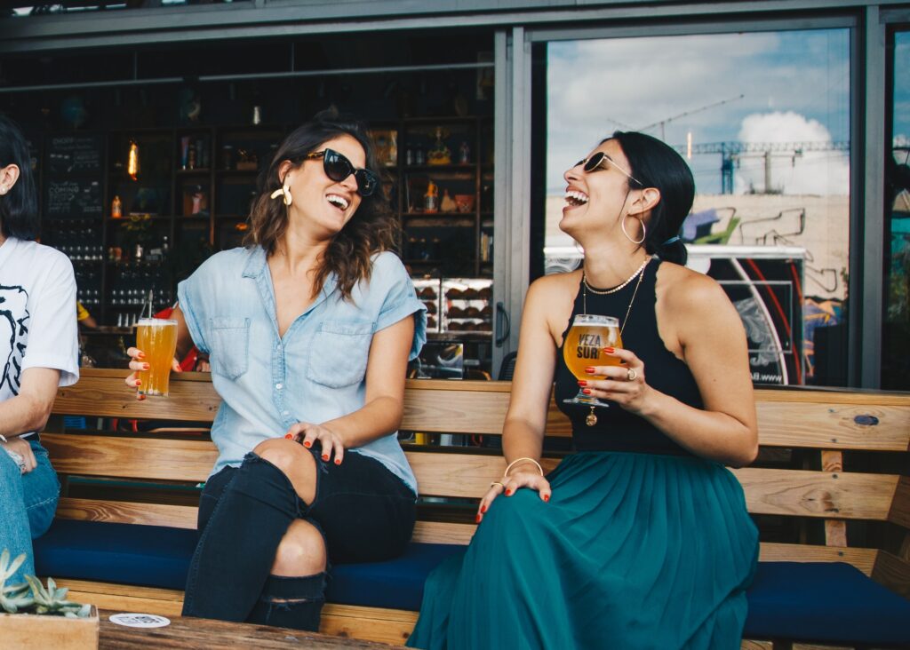 zwei frauen sitzen an einer bar, haben spaß und trinken bier