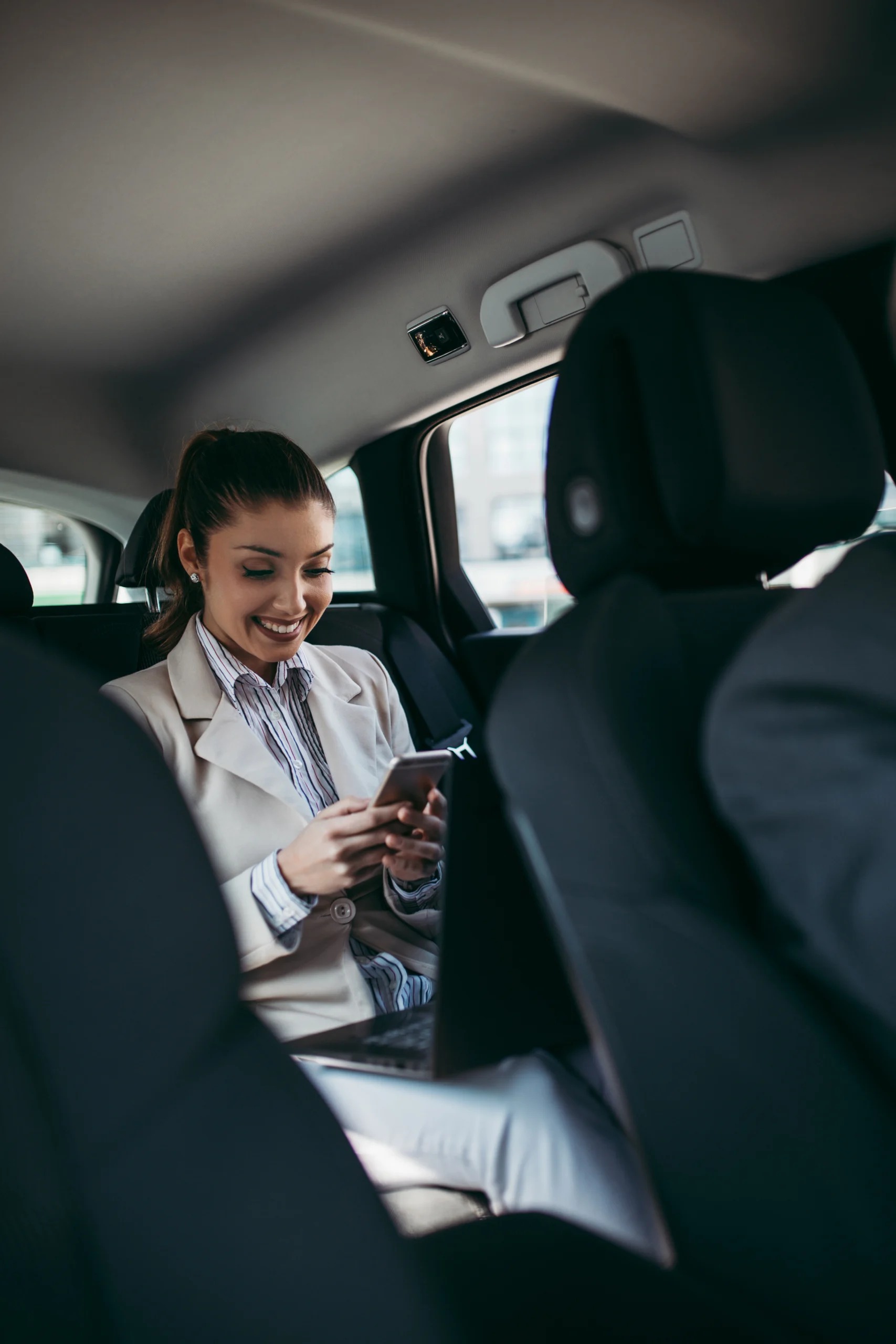 junge geschäftsfrau mit smartphone auf der rücksitzbank eines autos